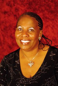 A black woman smiling in front of a red background.