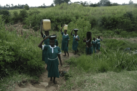 A group of girls carrying water jugs on a dirt path.