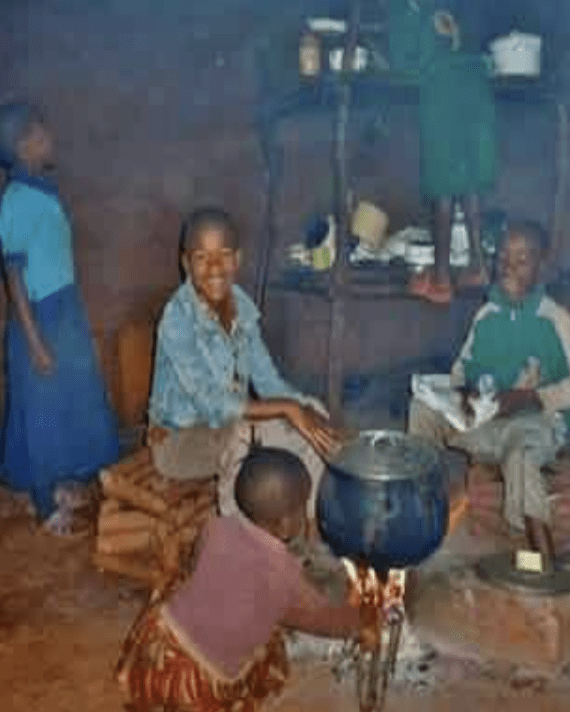 A group of children sitting around a stove in a hut.
