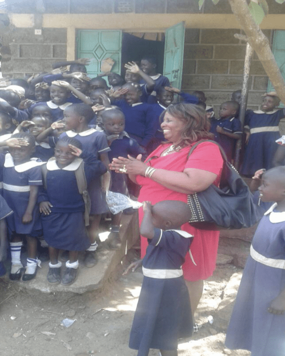 A woman in a red dress is standing in front of a group of children.